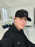 Velite Armor Performance Visor - Lightweight Style & Functionality worn by a man in a modern living room. Sleek black visor with embroidered logo, ideal for workouts or casual wear.