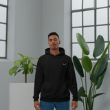 Velite Armor Premium Eco Hoodie in black, worn by a male model in a modern indoor setting with natural light and green plants. Sustainable activewear with minimalist design.