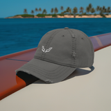 Velite Armor Premium Distressed Hat in gray, embroidered logo, showcased on a yacht deck with an ocean view, embodying a refined, adventure-driven lifestyle.