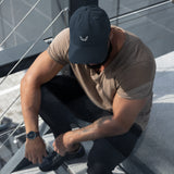 Man wearing the Velite Armor Black Distressed Dad Hat while sitting on outdoor stairs. The cap features an embroidered logo, breathable cotton fabric, and a vintage worn look, perfect for a stylish and active lifestyle.