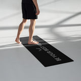 A person walking barefoot on a black yoga mat with the slogan “Be Your Best Version,” set in a minimalist indoor space with natural lighting.