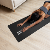 A woman performing a yoga stretch on a black Velite Armor mat with “Be Your Best Version” branding, inside a cozy home environment.