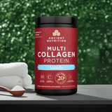  Jar of Ancient Nutrition Multi Collagen Protein Vanilla placed next to a wooden scoop and coconut, with a vibrant green plant wall in the background.