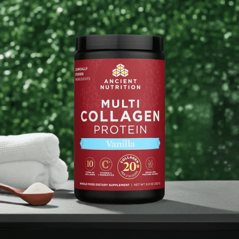  Jar of Ancient Nutrition Multi Collagen Protein Vanilla placed next to a wooden scoop and coconut, with a vibrant green plant wall in the background.