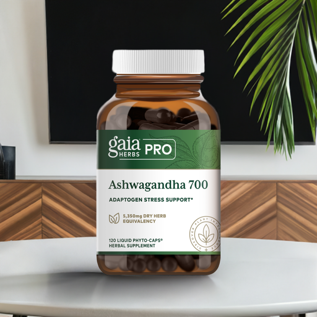 Gaia Herbs Pro Ashwagandha 700 bottle placed on a modern wooden table with a sleek black background and green plant leaves. The supplement provides adaptogenic stress support with 5,350 mg dry herb equivalency and comes in 120 liquid phyto-caps.