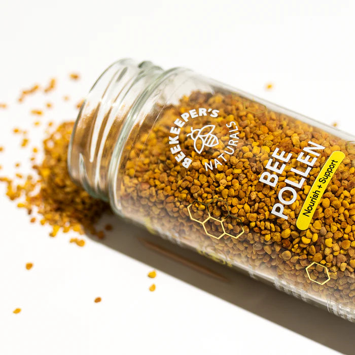 Beekeeper’s Naturals Bee Pollen jar tipped over, with pollen scattered on a white surface.