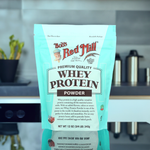 Bob's Red Mill Whey Protein Powder 12 oz pouch on kitchen counter, 14g protein per serving, unflavored, ideal for shakes and baking.