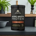 Two tubs of Equip Prime Protein Chocolate displayed on a counter with green plants in the background for a fresh, healthy vibe.