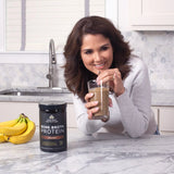 Woman smiling in her kitchen while drinking Equip Prime Protein shake, suggesting great taste and ease of use in daily routines.
