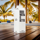 Boxed Water 500 ml – Pure & Sustainable Carton Packaging on a wooden deck with yoga mats and palm trees, emphasizing eco-friendly hydration outdoors.