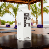 Boxed Water 500 ml – Pure & Sustainable Carton Packaging placed on a black table at a tropical outdoor yoga setting, promoting eco hydration.