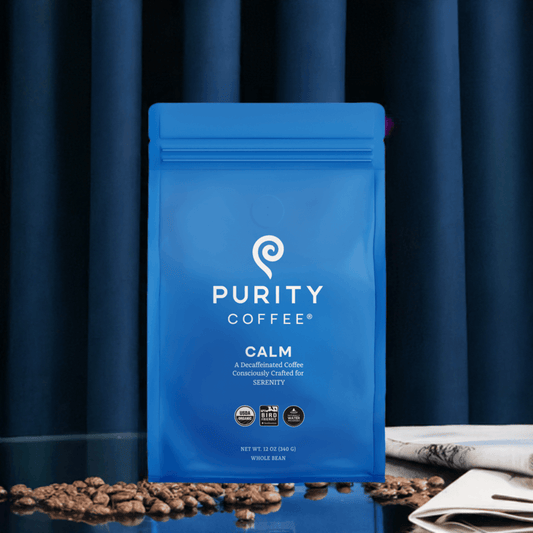 Organic Purity Coffee CALM: Decaf Whole Bean Coffee in blue resealable bag on table with scattered beans, ideal for a healthy caffeine-free brew.