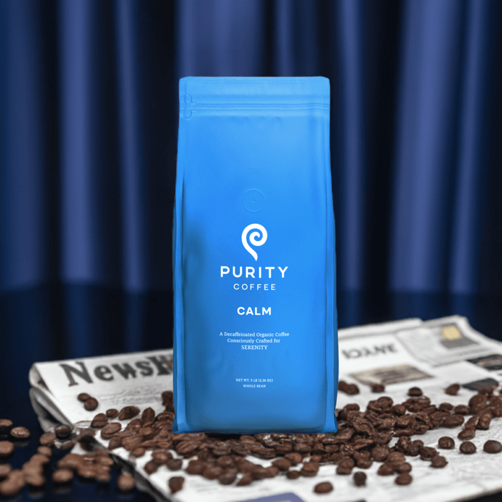 Purity Coffee CALM: Decaf Whole Bean Coffee bag standing on newspaper with coffee beans, showcasing organic, caffeine-free coffee for serenity.