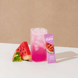 Refreshing glass of Cure Watermelon Hydration Mix with ice and watermelon slices on table

