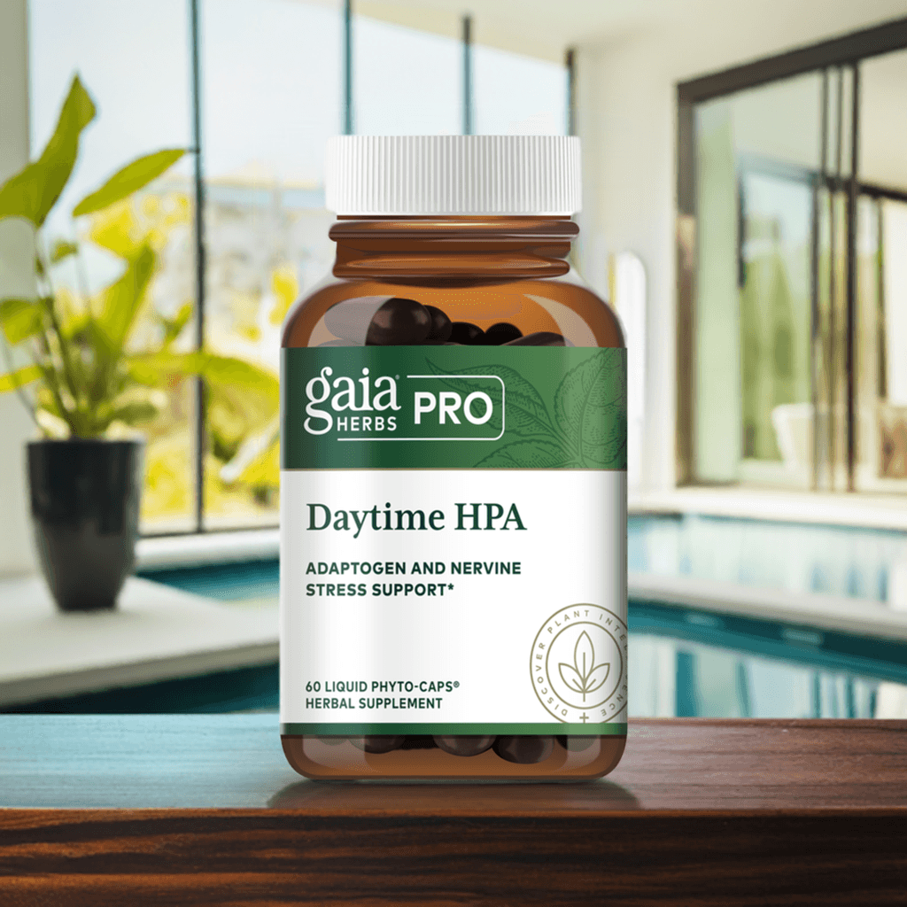 A bottle of Gaia Herbs PRO Daytime HPA supplement placed on a wooden surface with a background featuring a pool and lush green plants. The bottle is brown with a white cap and a green label highlighting its adaptogenic and nervine stress support benefits.