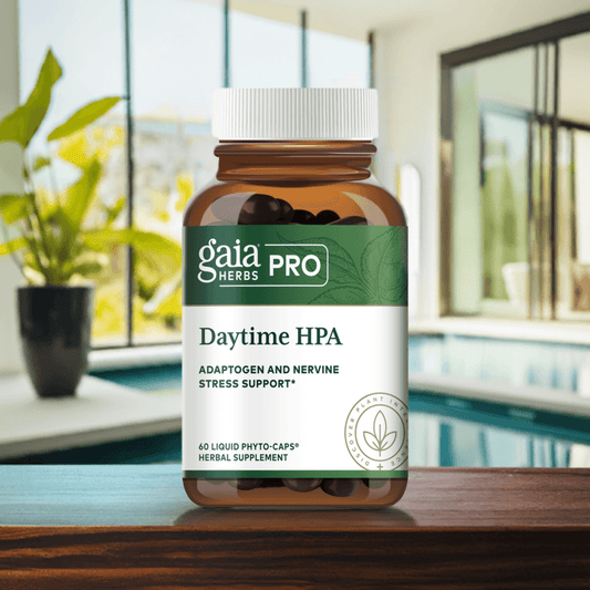 A bottle of Gaia Herbs PRO Daytime HPA supplement placed on a wooden surface with a background featuring a pool and lush green plants. The bottle is brown with a white cap and a green label highlighting its adaptogenic and nervine stress support benefits.