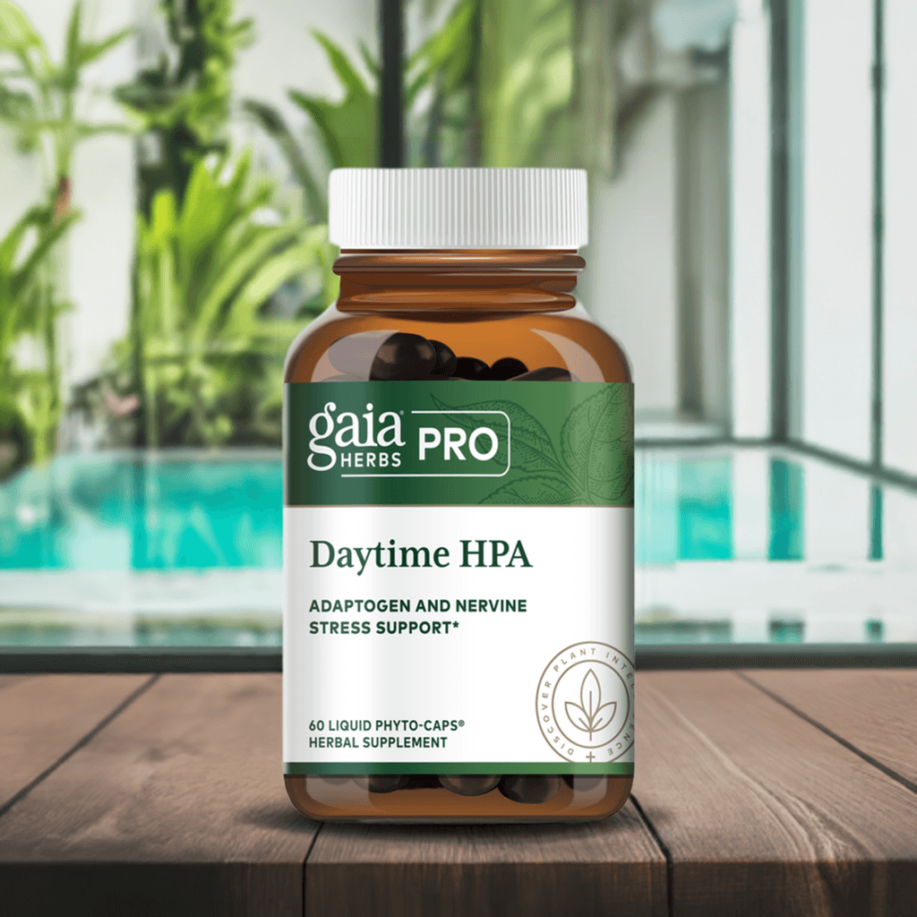 Gaia Herbs PRO Daytime HPA supplement bottle on a wooden table near a bright indoor space with a pool and greenery. The brown glass bottle with a white cap and green label promotes adaptogenic and nervine stress support.
