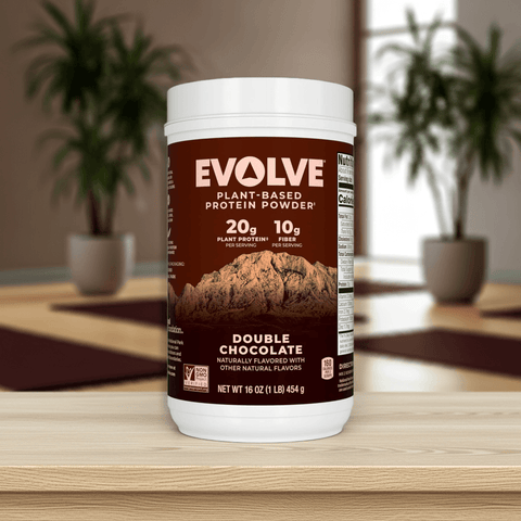 Evolve Protein Powder Classic Chocolate 1 lb tub on wooden table with indoor plants, plant-based protein