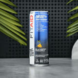 FitAid Energy Blackberry Pineapple can placed next to tropical green leaves on a black reflective surface.

