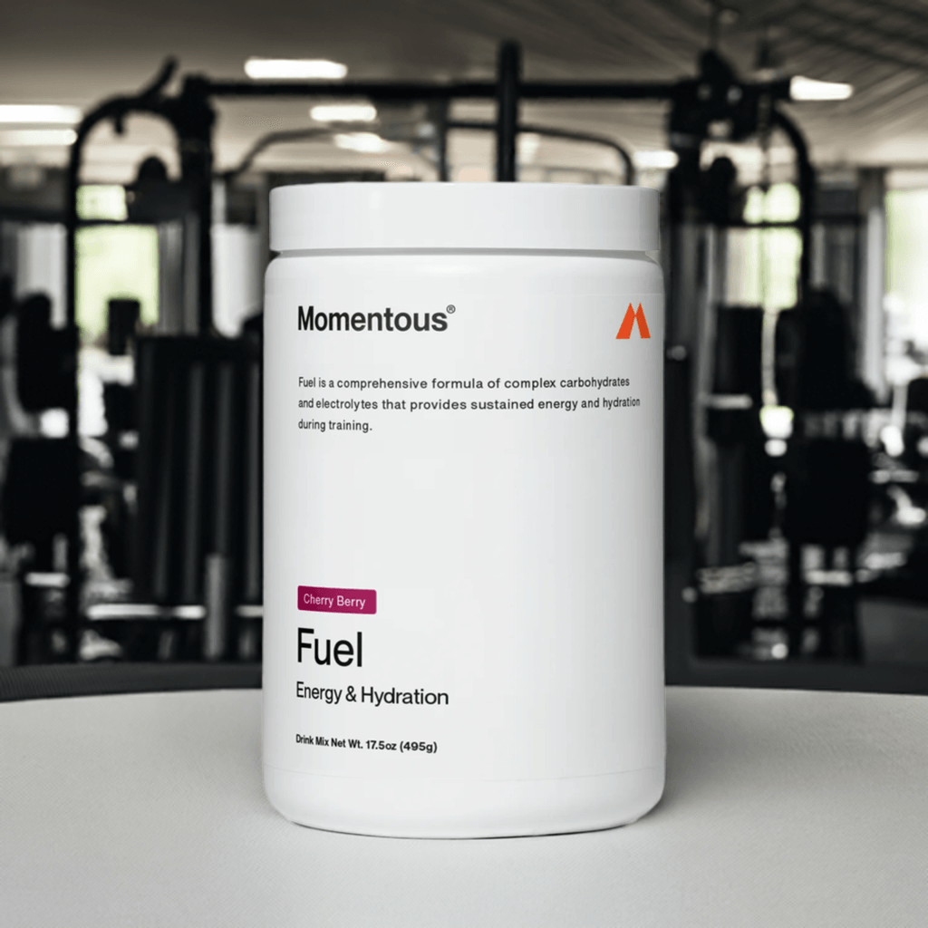 Paquete de bebida en polvo Momentous Fuel, sabor Cherry Berry, diseñado para proporcionar energía sostenida e hidratación durante el entrenamiento. El envase destaca que contiene carbohidratos complejos y electrolitos, con un peso neto de 17.5 oz (49 g). Ideal para deportistas que buscan un rendimiento óptimo.
