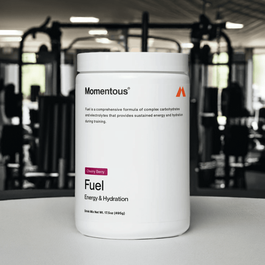 Paquete de bebida en polvo Momentous Fuel, sabor Cherry Berry, diseñado para proporcionar energía sostenida e hidratación durante el entrenamiento. El envase destaca que contiene carbohidratos complejos y electrolitos, con un peso neto de 17.5 oz (49 g). Ideal para deportistas que buscan un rendimiento óptimo.