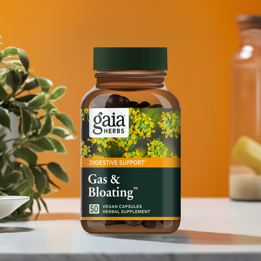Gaia Herbs Gas & Bloating supplement bottle, designed for digestive support. The brown glass container with a green cap features a label decorated with yellow flowering herbs. The product contains 50 vegan capsules and is classified as a herbal supplement. The background has warm orange tones with natural elements.