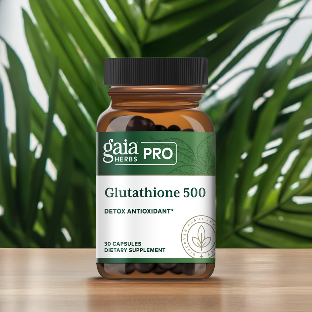 Gaia Herbs PRO Glutathione 500 dietary supplement bottle with detox antioxidant formula, featuring 30 capsules, placed on a wooden surface with green tropical leaves in the background. / Suplemento dietético Gaia Herbs PRO Glutathione 500 con fórmula antioxidante para detox, contiene 30 cápsulas, colocado sobre una superficie de madera con hojas tropicales verdes de fondo.