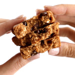Close-up of a hand breaking a GoMacro Peanut Butter Chocolate Chip bar, showing chewy texture and natural ingredients.