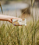 Hand holding a GoMacro bar outdoors in a wheat field – wholesome, organic, and perfect for on-the-go energy.