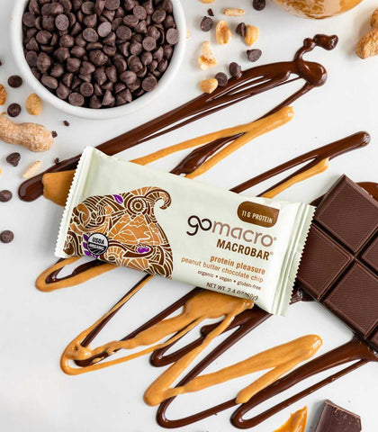 GoMacro Peanut Butter Chocolate Chip bars surrounded by chocolate chunks, chips, and peanut butter drizzle – plant-based protein snack.