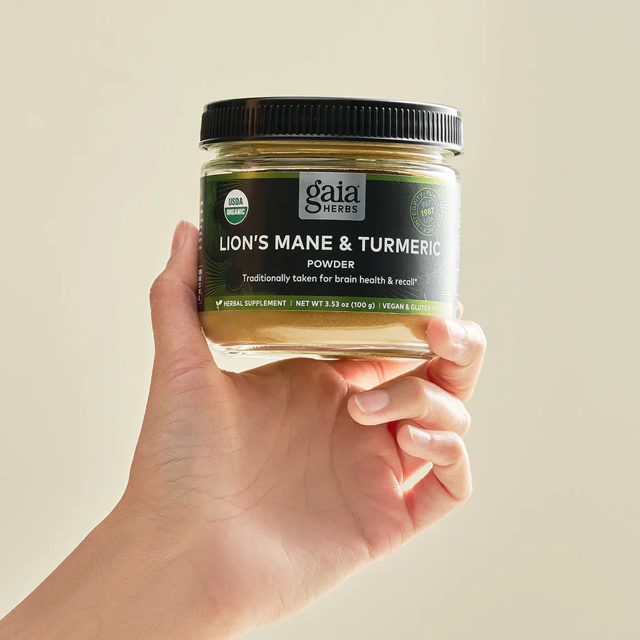 Hand holding Gaia Herbs Lion's Mane & Turmeric - 3.5 oz powder jar, a vegan and gluten-free brain health supplement for cognitive support.