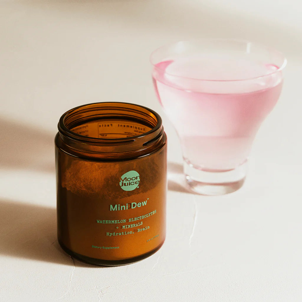 Mini Dew electrolyte and mineral powder in amber jar next to a glass of pink hydration drink for brain and body wellness.