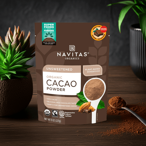 Front-facing black cacao powder pouch on a kitchen counter with fresh plants and a wooden spoon.

