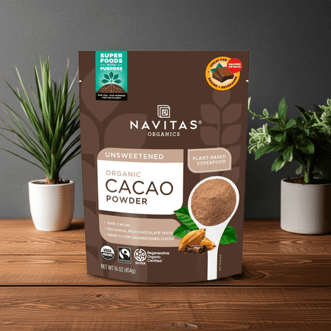 Navitas Organic Cacao Powder pouch displayed on a wooden surface with plants in the background.