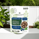 Navitas Organics Power Snacks Blueberry Hemp pouch on outdoor table surrounded by green plants – healthy superfood energy bites


