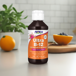 Nature’s Plus Ultra B-12 Liquid Supplement bottle on a kitchen counter with oranges, blueberries, and leafy greens in the background, suggesting vitality and wellness.