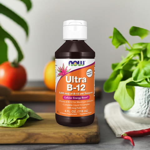 Nature’s Plus Ultra B-12 Liquid Supplement bottle on a wooden board surrounded by fresh spinach, tomatoes, and basil, promoting a healthy lifestyle.