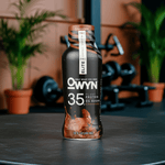 OWYN Pro Elite Plant Protein Shake – Chocolate flavor 35g bottle with gym equipment and plants in background.
