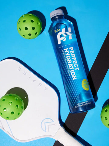 Perfect Hydration Alkaline Water 1L bottle with pH 9.5+, shown next to pickleball paddles for active lifestyle hydration.

