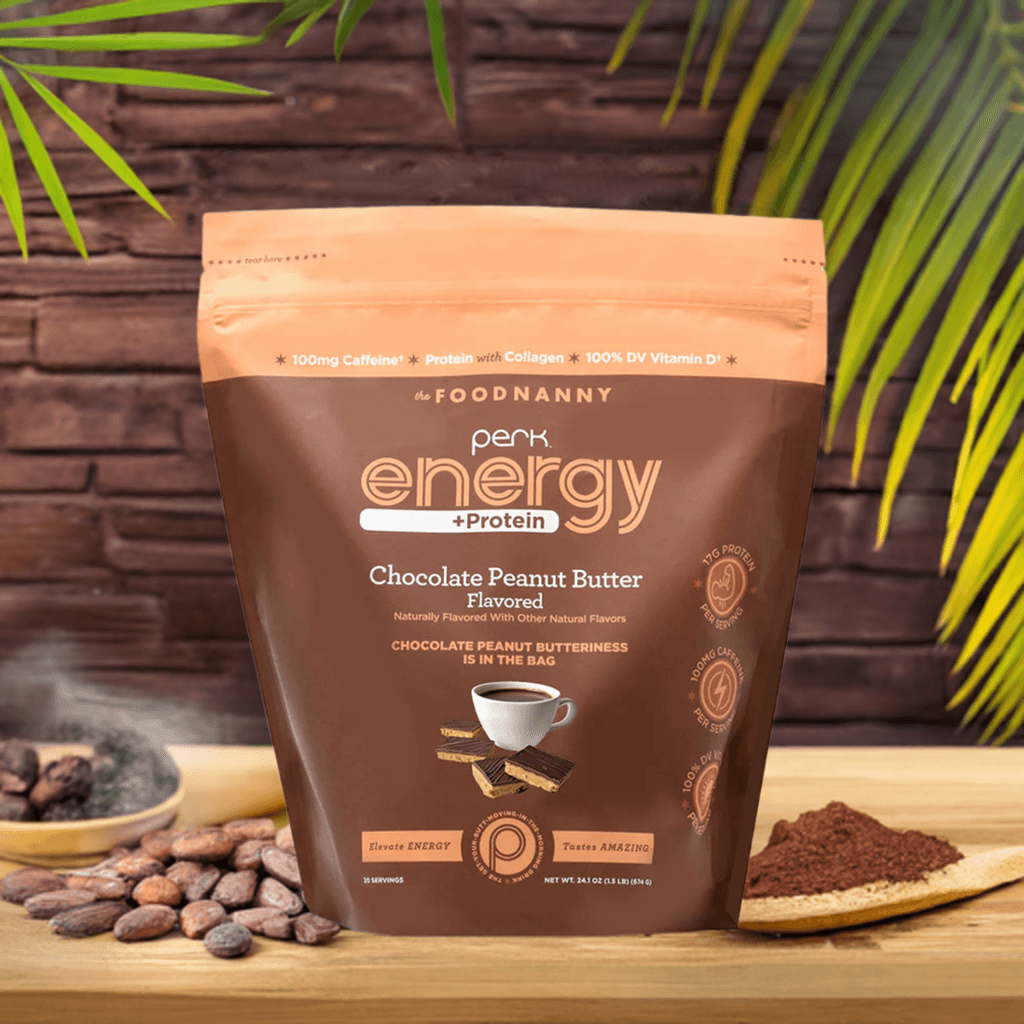 Perk Energy + Protein – Chocolate Peanut Butter pouch on a wooden surface with a tropical background featuring palm leaves, cocoa beans, and cocoa powder, highlighting its natural and rich ingredients.