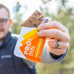 Man holding Probar Oatmeal Chocolate Chip bar outdoors, perfect on-the-go energy snack for hiking and adventure
