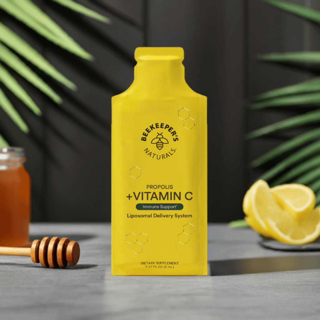 Propolis + Vitamin C Liposomal by Beekeeper's Naturals in a bright yellow pouch, shown with honey dipper, lemon slices, and honey jar for immune support.