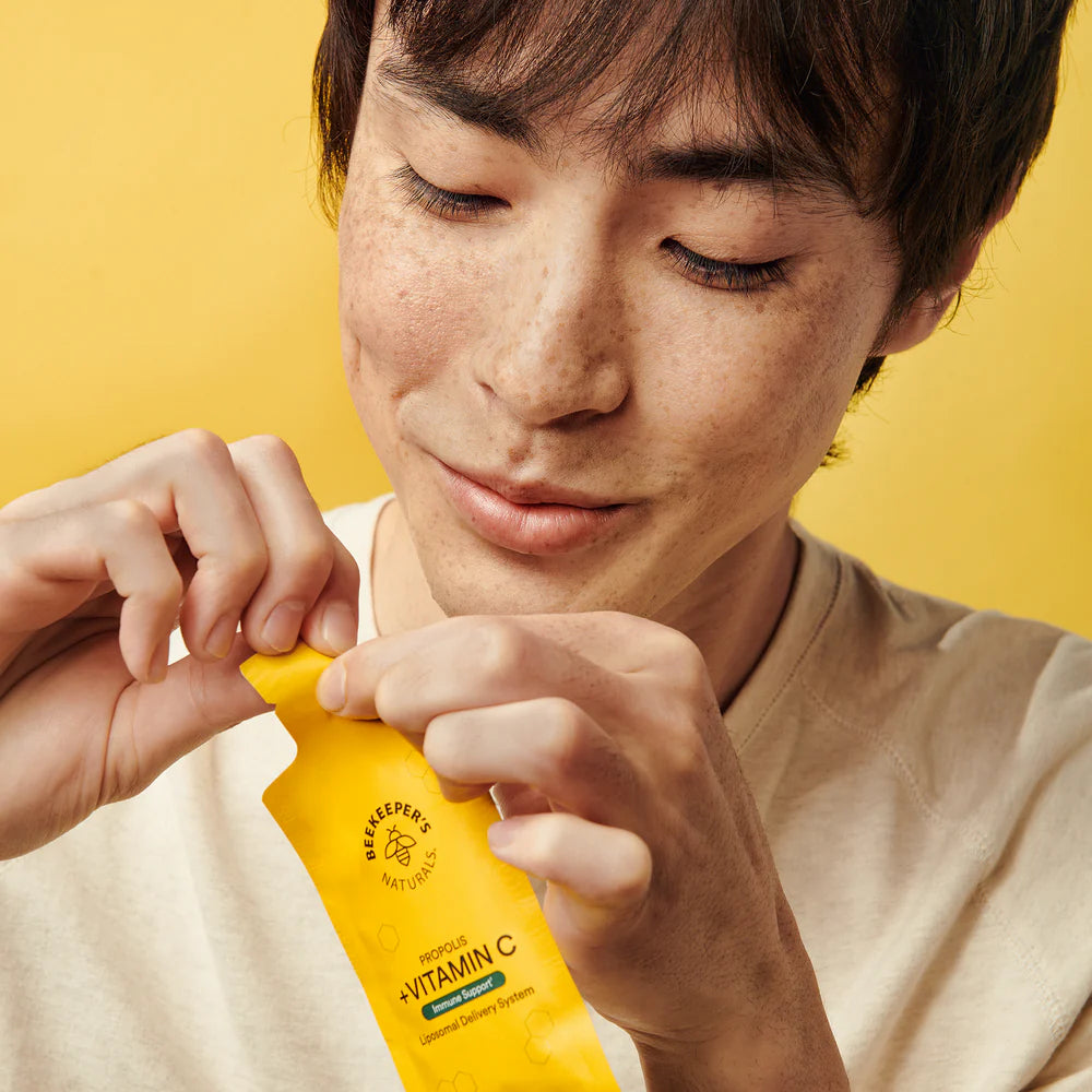 Joven disfrutando de Beekeeper’s Naturals Propolis + Vitamin C, un suplemento liposomal para el soporte inmunológico. Imagen con fondo amarillo vibrante que refleja energía y bienestar.