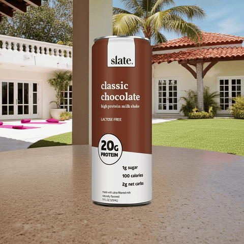 Slate Milk Classic Chocolate Shake can placed outdoors by the pool in a tropical setting, highlighting its refreshing protein-packed benefits.