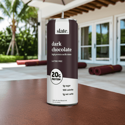 Slate Milk Dark Chocolate Shake can on outdoor table with poolside view, high-protein lactose-free chocolate milk.