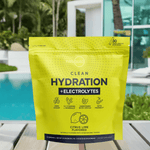 Citrus Lime Clean Hydration + Electrolytes pouch on a poolside table with tropical greenery and a luxury house in the background.