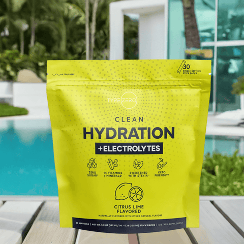 Citrus Lime Clean Hydration + Electrolytes pouch on a poolside table with tropical greenery and a luxury house in the background.