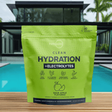 Clean Hydration + Electrolytes pouch displayed poolside with a sleek black glass-front house and tropical plants behind it, emphasizing a luxurious healthy lifestyle.
