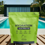 Green Clean Hydration + Electrolytes pouch placed on sunlit deck with pool and modern house in the background, promoting hydration for active summer living.