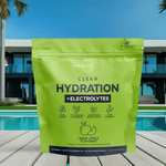 Front view of Clean Hydration + Electrolytes green pouch placed on a wooden deck by a pool, with a modern villa and palm trees in the background.